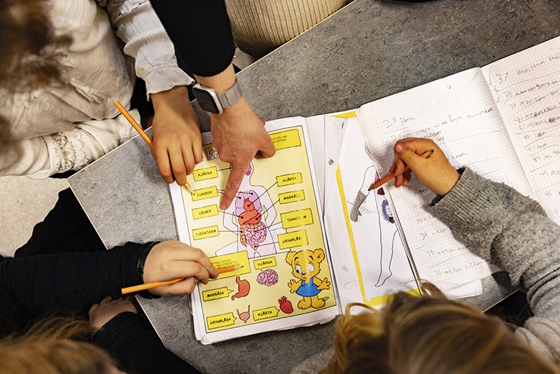 Bild från klassrum med lärare och elever i grundskolan tittar i ett arbetsmaterial