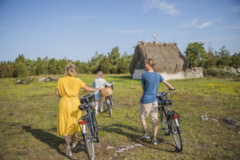 Tre personer leder sina cyklar framför ett lambgift på Fårö